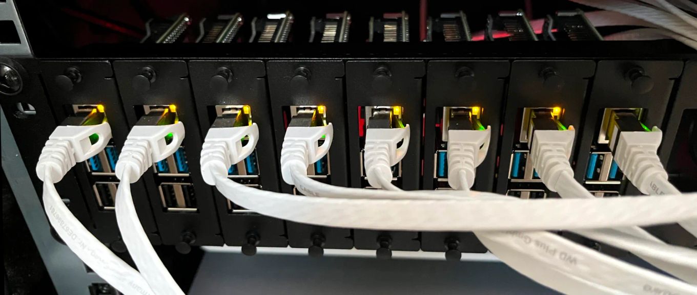 A black 19 inch rack with 8 vertically mounted Raspberry Pi computers each connected with a flat, white Ethernet cable to a switch outside of the picture.